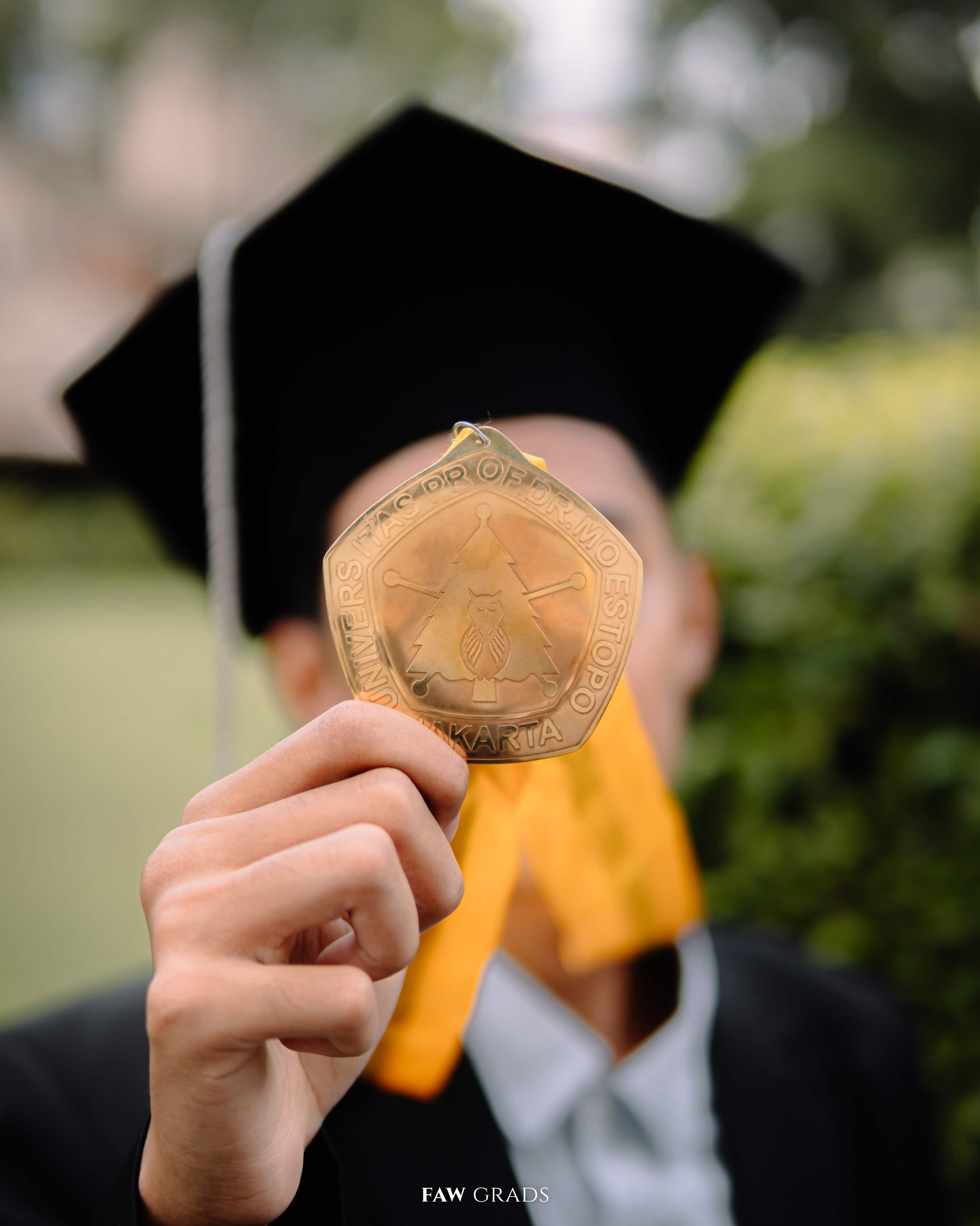 Potret wisuda hitam putih sarjana ekonomi berbaring di rumput sambil memegang topi toganya
